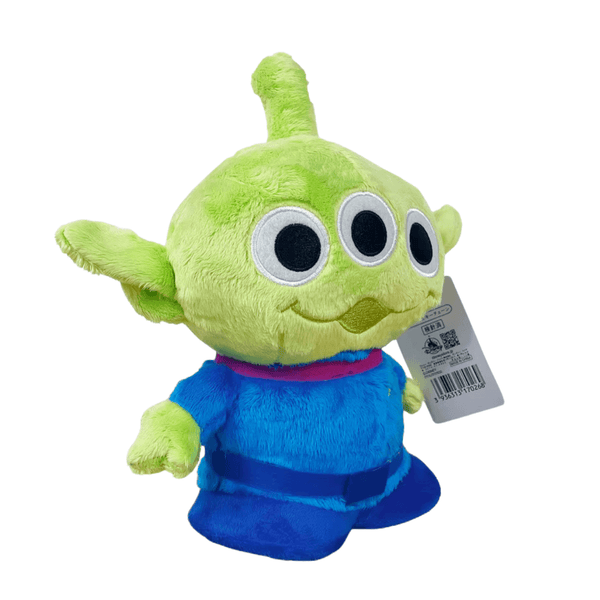 peluche Alien verte en tissu doux, avec trois grands yeux noirs cerclés de blanc et une combinaison bleue