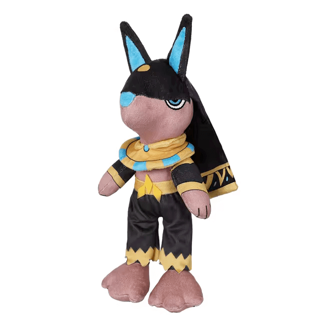 Peluche Anubis aux oreilles noires et bleues, avec foulard doré et bleu, pantalon noir et cape ornée de motifs égyptiens.