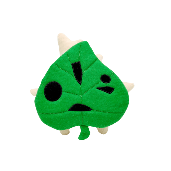 Peluche Korogu en tissu vert, avec un visage formé de motifs noirs et de petites excroissances beige clair.