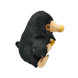 Peluche Niffleur noire à poils doux, avec un long bec beige, des pattes claires et un objet doré dans les mains.